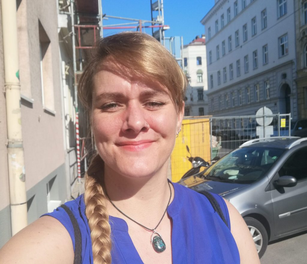 Das Bild zeigt ein Selfie von Lorena Hoormann auf der Straße, im Hintergrund ist ein Auto und eine Baustelle zu sehen. Der Himmel ist blau, die Sonne scheint.