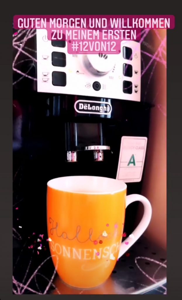 Das Bild zeigt eine orangenen Becher mit der Aufschrift Hallo Sonnenschein, unter der Kaffeemaschine von de Longhi.