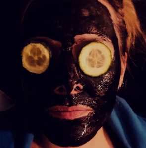Nahaufnahme eines Gesichts mit schwarzer Gesichtsmaske und Gurkenscheiben auf den Augen