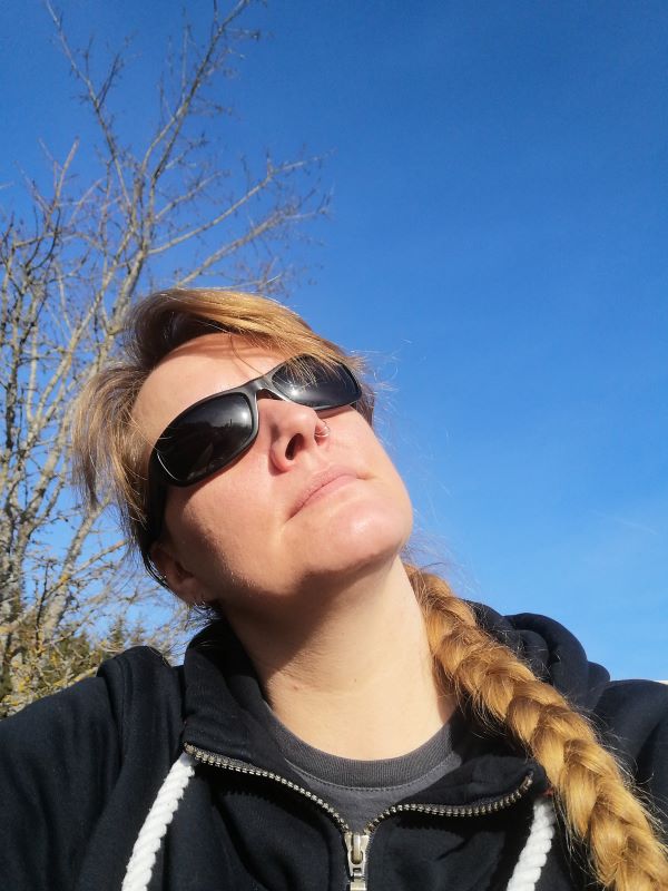 Porträtaufnahme, Lorena sitzt mit einer Sonnenbrille, das Gesicht der Sonne zugewandt und genießt scheinbar die Wärme.