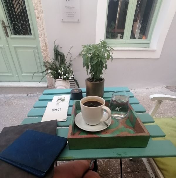 Aus Sichtweise von Lorena, sieht man einen Kaffeetisch an dem sie allein sitzt, mit Buch und Schreibzeug.