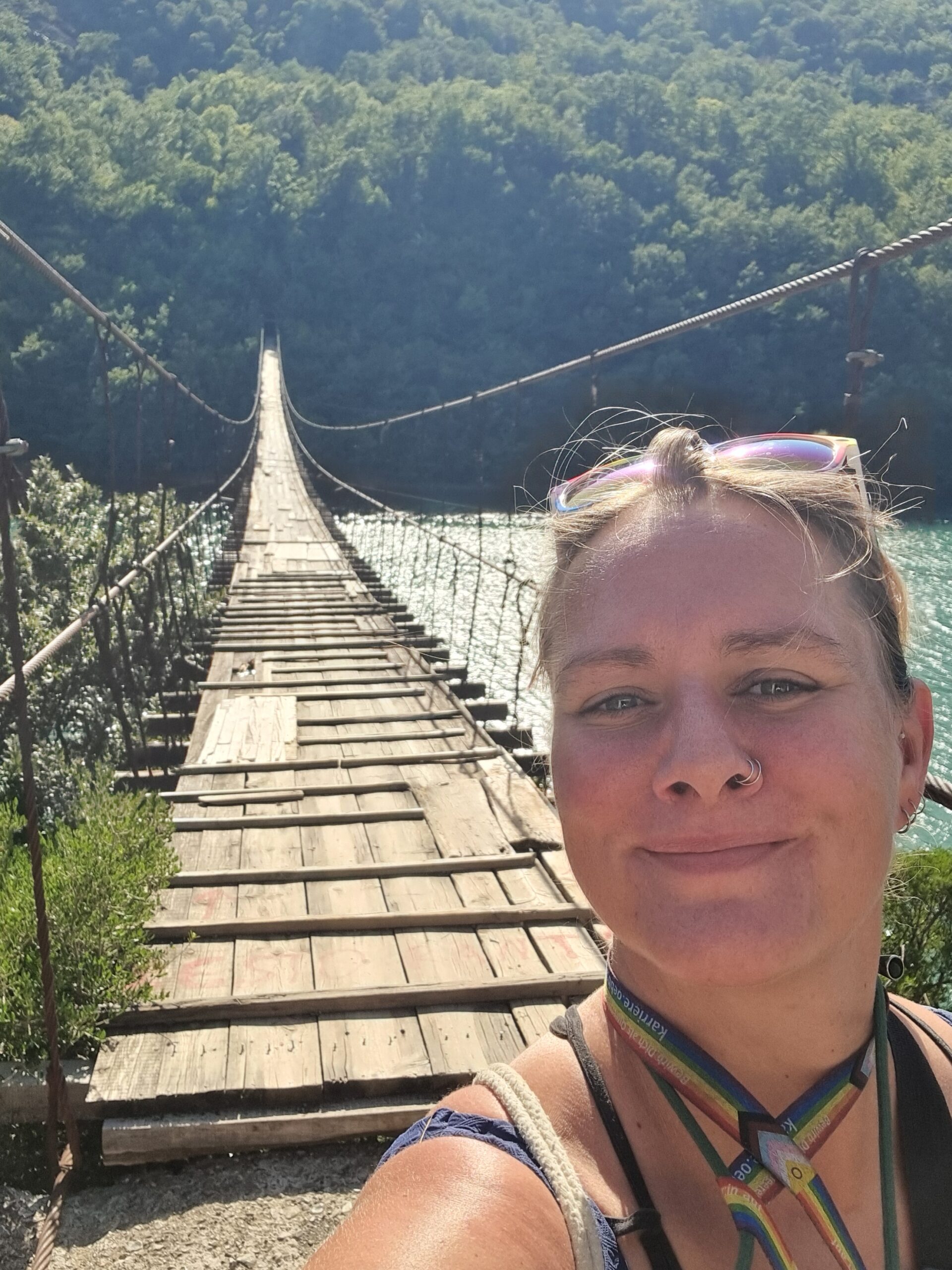 Frau steht auf einer schmalen Hängebrücke über Wasser, Blick nach vorne, Symbol für Übergang und Neubeginn