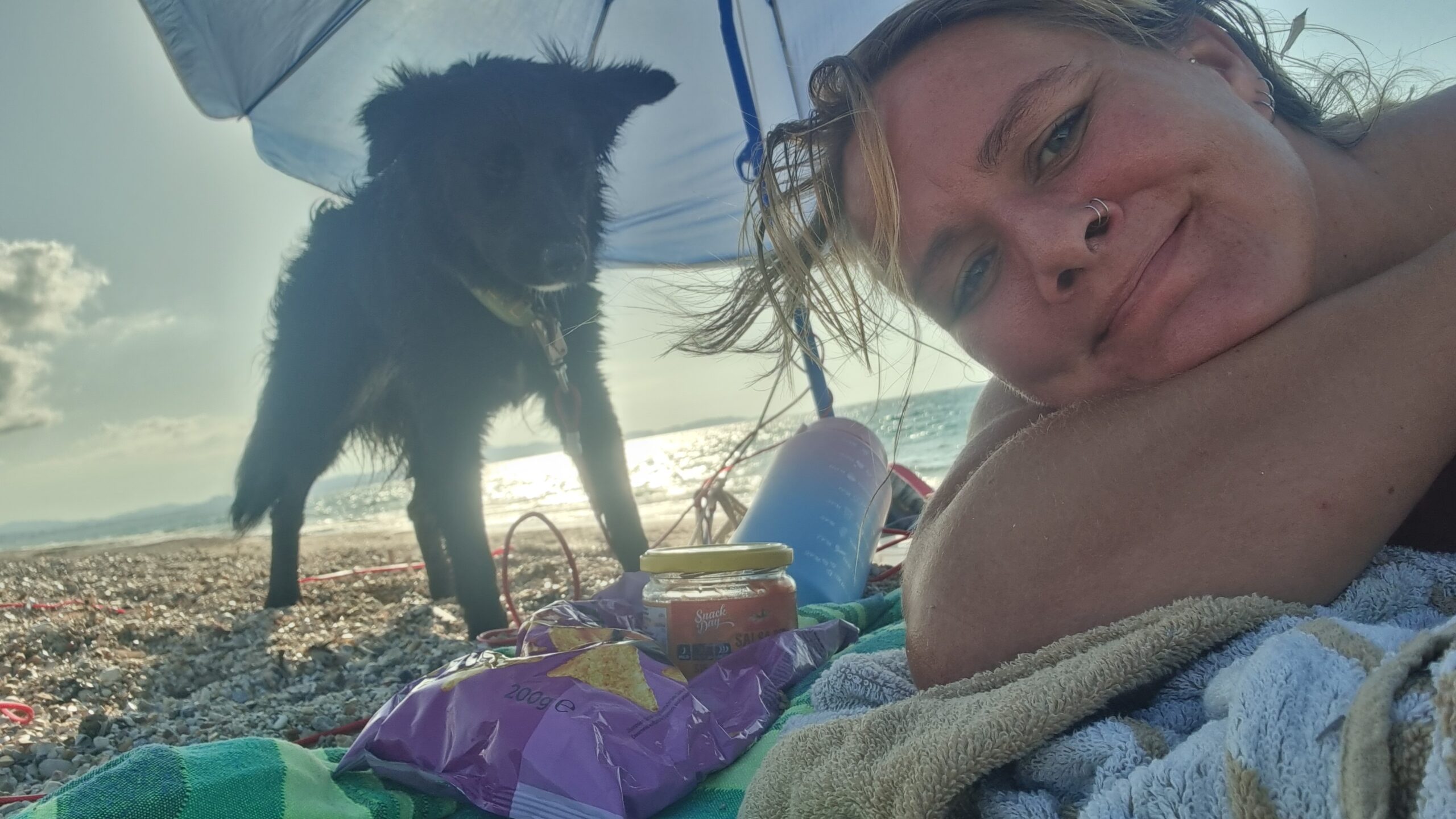 Frau liegt entspannt am Strand mit Hund, Meer im Hintergrund, Symbol für Ruhe, Verbundenheit und Ankommen
