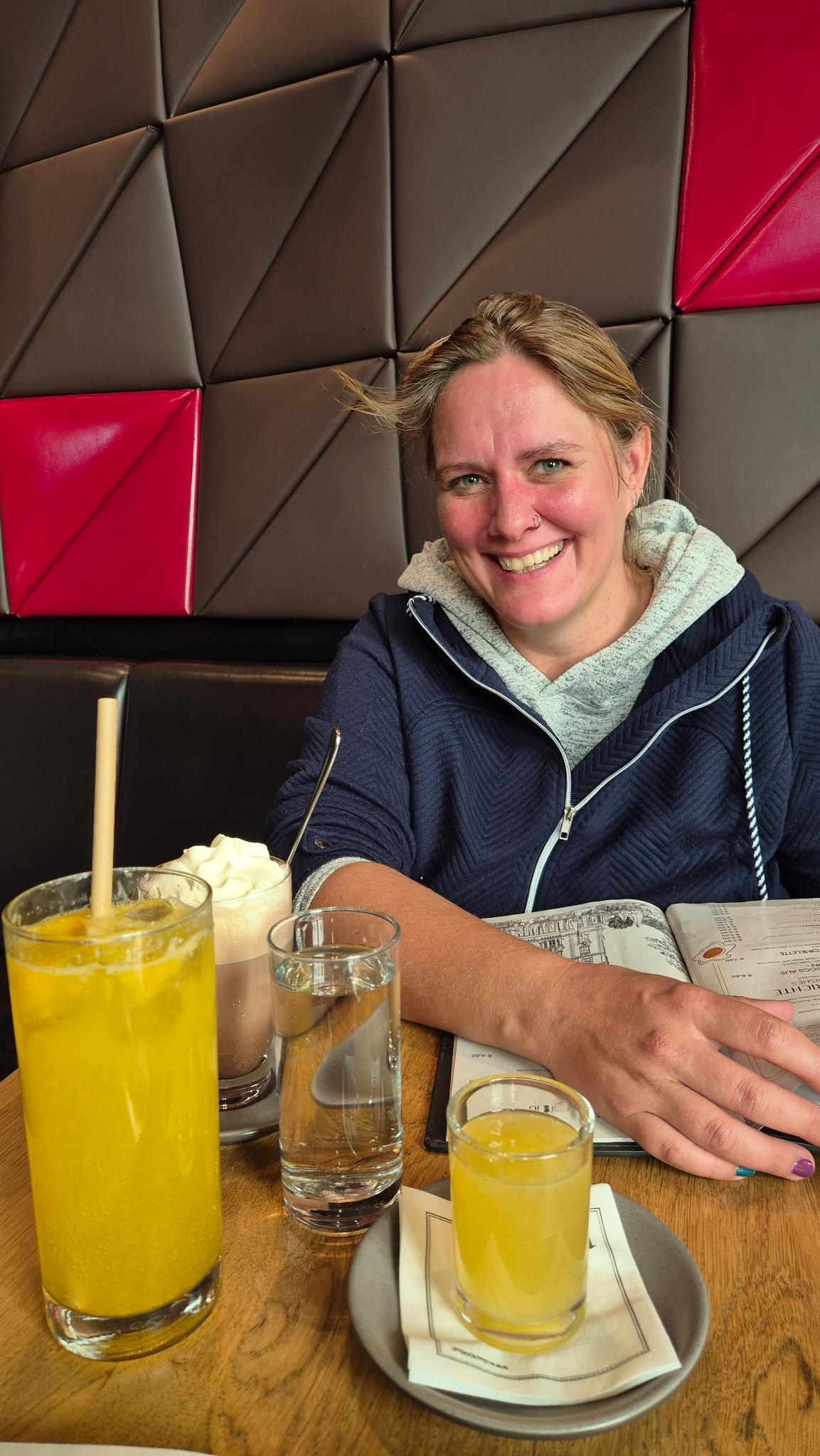 Frau sitzt entspannt im Café, lächelt, Alltagsszene mit Getränken